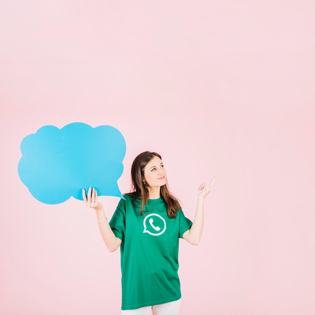 Free photo woman pointing upwards holding empty blue speech bubble