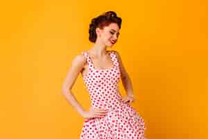 Free photo woman in polka-dot dress posing with smile. romantic pinup girl laughing on yellow space.