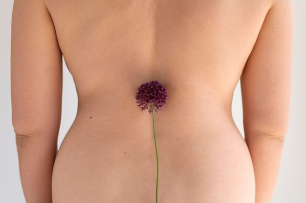 Free photo woman posing confidently in the nude and showing back with flower