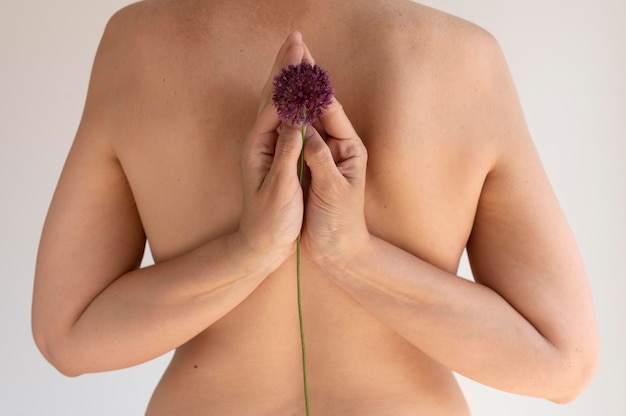 Free photo woman posing confidently in the nude and showing back with flower