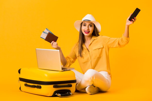 Woman posing next to luggage while holding smartphone and plane tickets