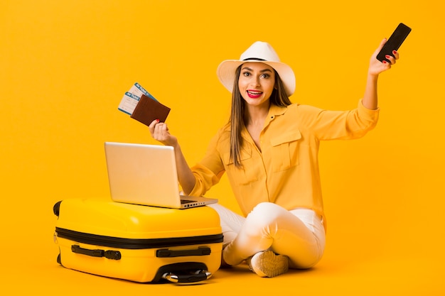 Woman posing next to luggage while holding smartphone and plane tickets