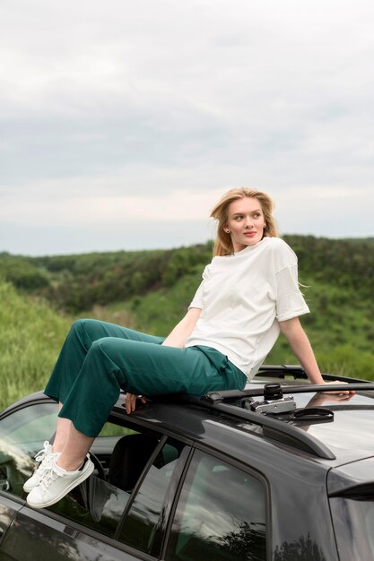 Woman posing in nature while standing on top of car