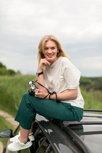 Woman posing on top of car while holding camera