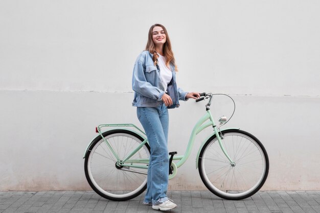 Женщина позирует, держа свой велосипед на открытом воздухе в городе