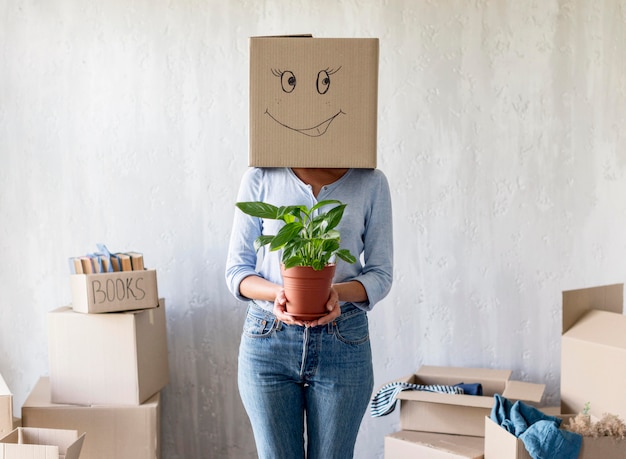 植物を手で押しながらポーズをとる女性と引越日の頭上のボックス