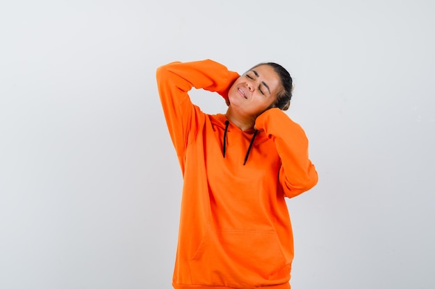 Woman posing with hands behind head in orange hoodie and looking peaceful