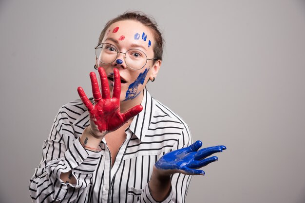 Woman posing with paints on her face on gray background . 