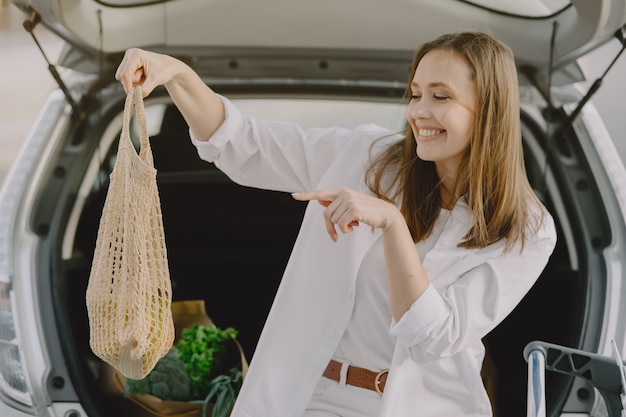 女性が彼女の車で買い物袋でポーズ