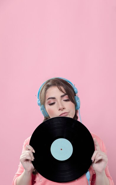 Woman posing with vinyl record while wearing headphones and copy space