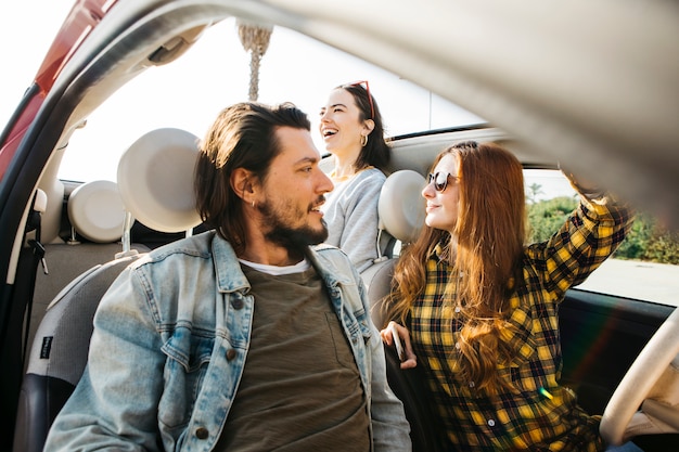 Foto gratuita donna e uomo positivo che si siedono in automobile vicino alla signora sorridente che si appoggia fuori dall'auto