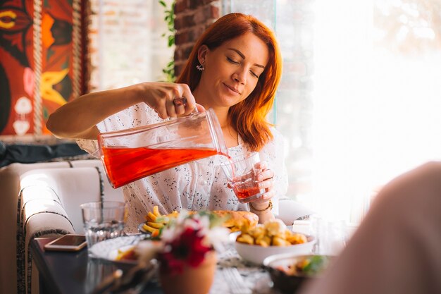 Woman pouring beverage into glass from jar served for lunch at cafe