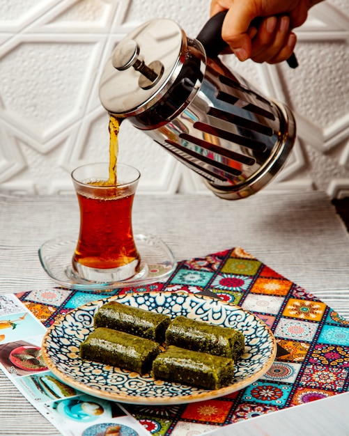 Free photo woman pouring black tea from french press served with turkish dessert