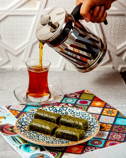 Woman pouring black tea from french press served with turkish dessert