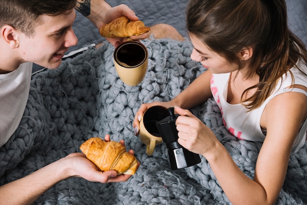 Woman pouring coffee in cup on bed 