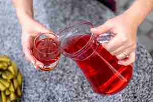 Free photo woman pouring healthy cranberry juice from bottle into glass