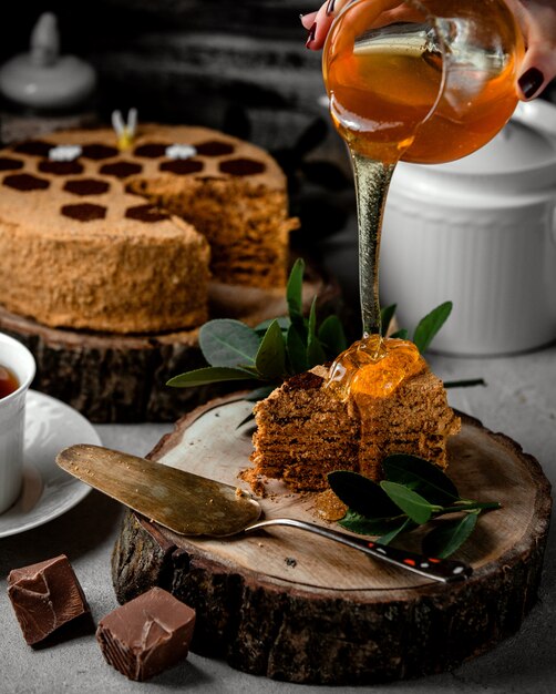 Woman pouring honey over honey cake with chocolate cream