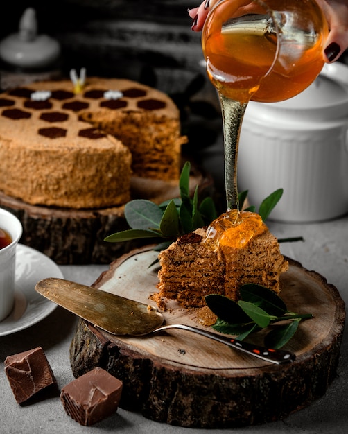 チョコレートクリームと蜂蜜ケーキに蜂蜜を注ぐ女性