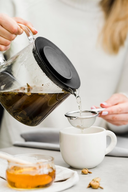 Foto gratuita tè di versamento della donna in tazza dal produttore di tè usando il setaccio