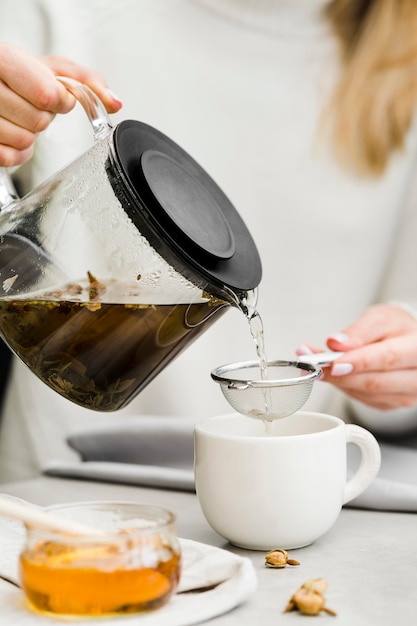 Woman pouring tea in cup from tea brewer using sieve