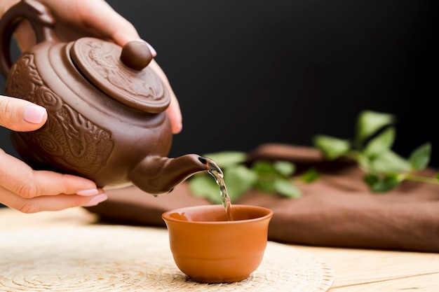 Woman pouring tea from clay teapot in clay teacup