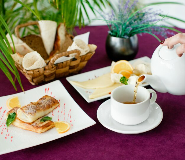 Woman pouring tea from teapot for breakfast with crepes