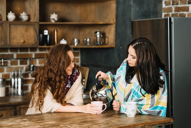 Woman pouring tea for her female friend in kitchen