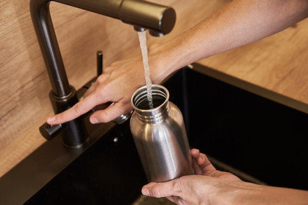 Woman pouring water in metal eco friendly bottle. zero waste concept Premium Photo