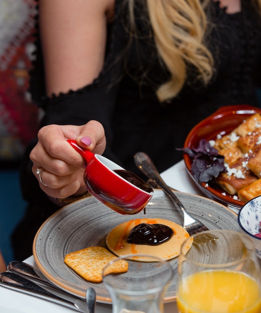 woman pours in jam on pancake for breakfast