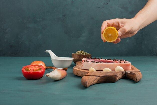 Woman pours lemon juice into the a piece of uncooked meat on blue table.