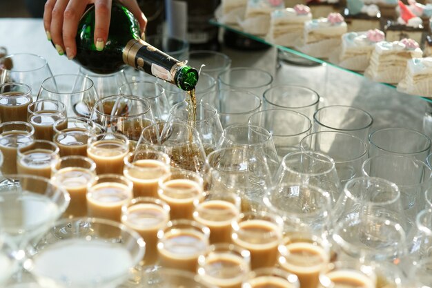 Woman pours whisky in glasses on table with sweets and alcohol 