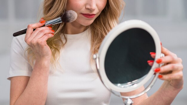 Woman powdering face while holding mirror