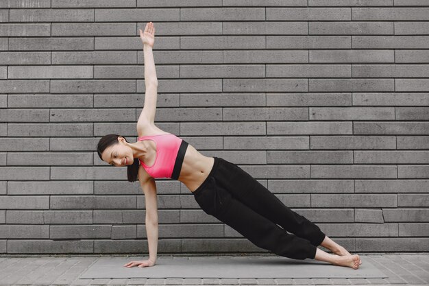 Woman practicing advanced yoga against a dark urban wall