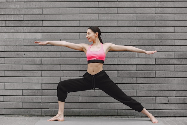 Woman practicing advanced yoga against a dark urban wall