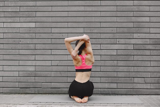 Woman practicing advanced yoga against a dark urban wall