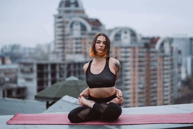 Woman practicing yoga on the mat on the roof and doing yoga exercises