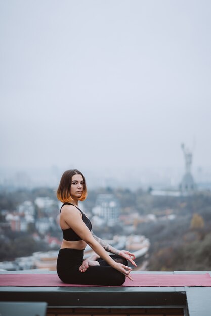 Woman practicing yoga on the mat on the roof and doing yoga exercises