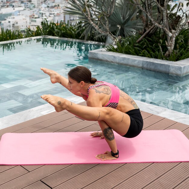 Woman practicing yoga position by the pool outdoors