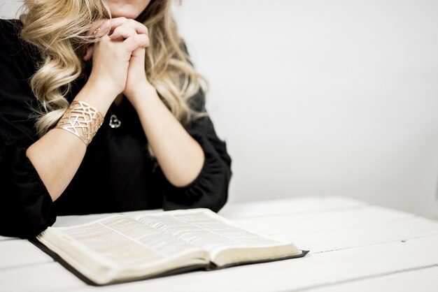 Женщина молится с тесно связанными пальцами возле открытой книги на столе