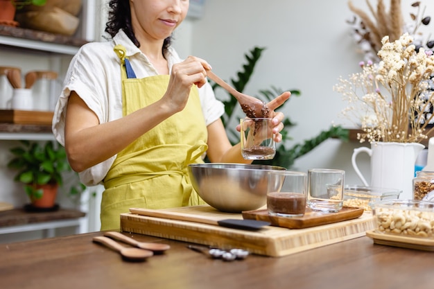 Женщина готовит пудинг с чиа на кухне, выкладывая нижний слой из миндального молока, какао и семян чиа.