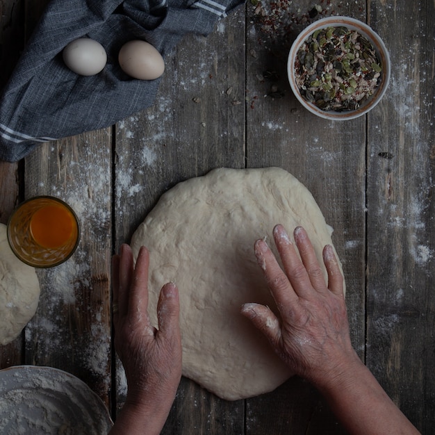 Woman preparing dough with hands for shaping on wooden table top view