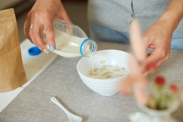 집에서 건강한 아침 식사를 준비하는 여성, 시리얼 그래놀라 플레이크 그릇에 우유를 붓는 여성 손, 견과류 씨앗 건포도, 홈 뮤즐리 음식 귀리 식사, 라이프스타일 개념
