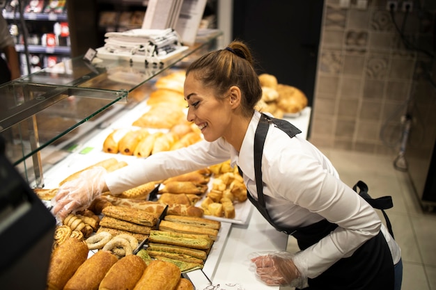 Woman preparing pastry for sale in supermarket bakery department