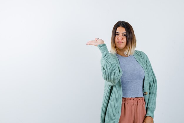 Woman pretending to show something in casual clothes and looking serious. front view.