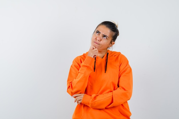 Woman propping chin on hand in orange hoodie and looking hesitant