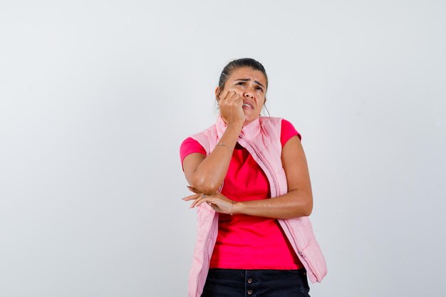 Woman propping chin on hand in t-shirt, vest and looking sad