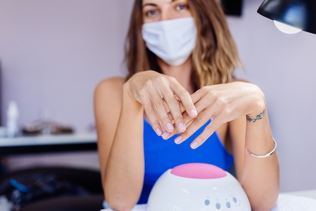 Woman in protective medical mask in beauty salon hold palette and select a color Manicure procedure nail care grand opening Quarantine is over Small businessess are open again