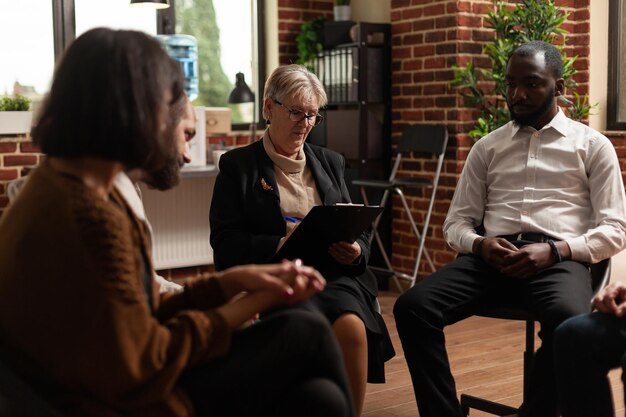 Woman psychologist giving rehab advice to people at aa group therapy session. Therapist meeting with patients dealing with mental health problems for rehabilitation and guidance.