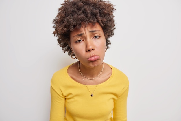 Foto gratuita la donna porta le labbra sembra infelicemente sconvolta o lunatica facce problemi vestiti con un maglione giallo casual isolato su bianco ha deluso il viso. concetto di emozioni negative