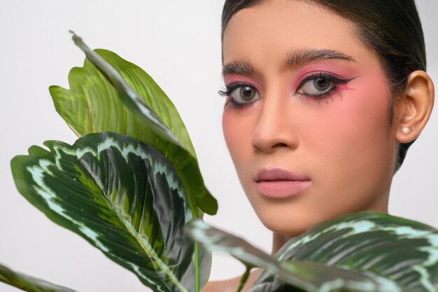 Woman put on pink makeup and decorated with leaves isolated on white